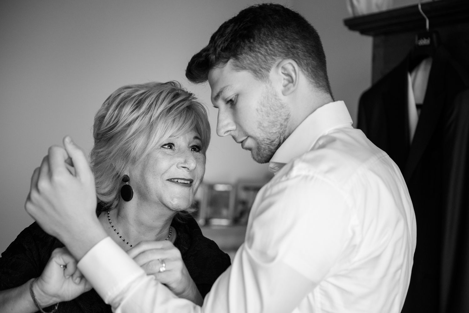 Black and white photo of a groom in a white shirt sharing a tender moment with an older woman.