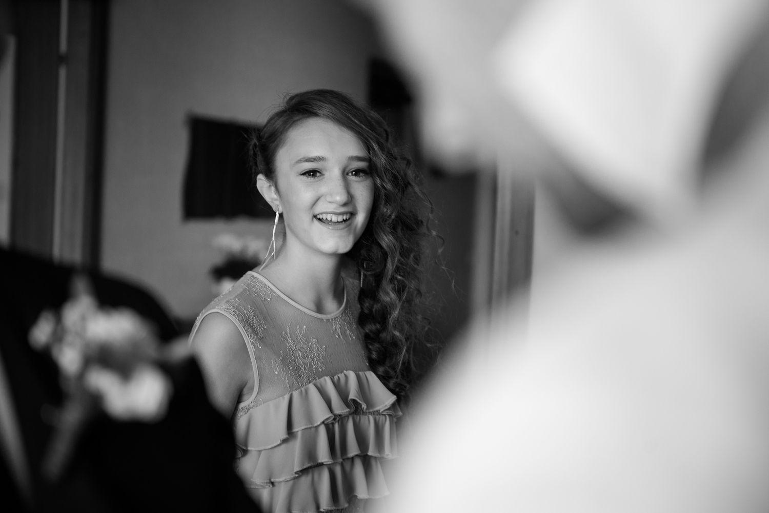 Black and white photo of a young girl smiling joyfully at a wedding celebration.
