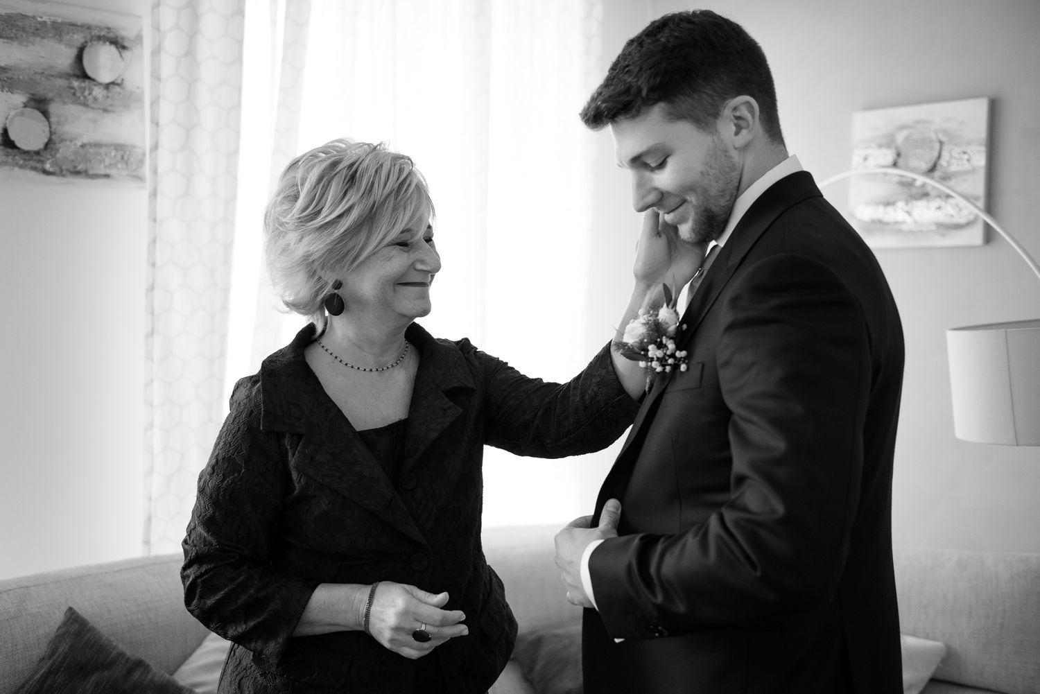 Black and white photo of a mother pinning boutonniere on her son the groom.