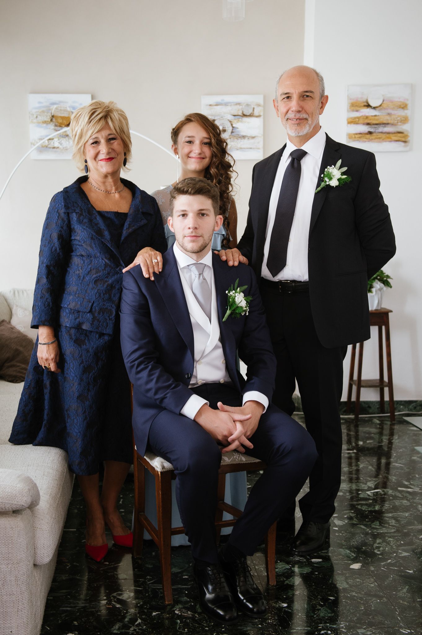 Groom in navy suit poses with his family for a formal wedding portrait in an elegant room.