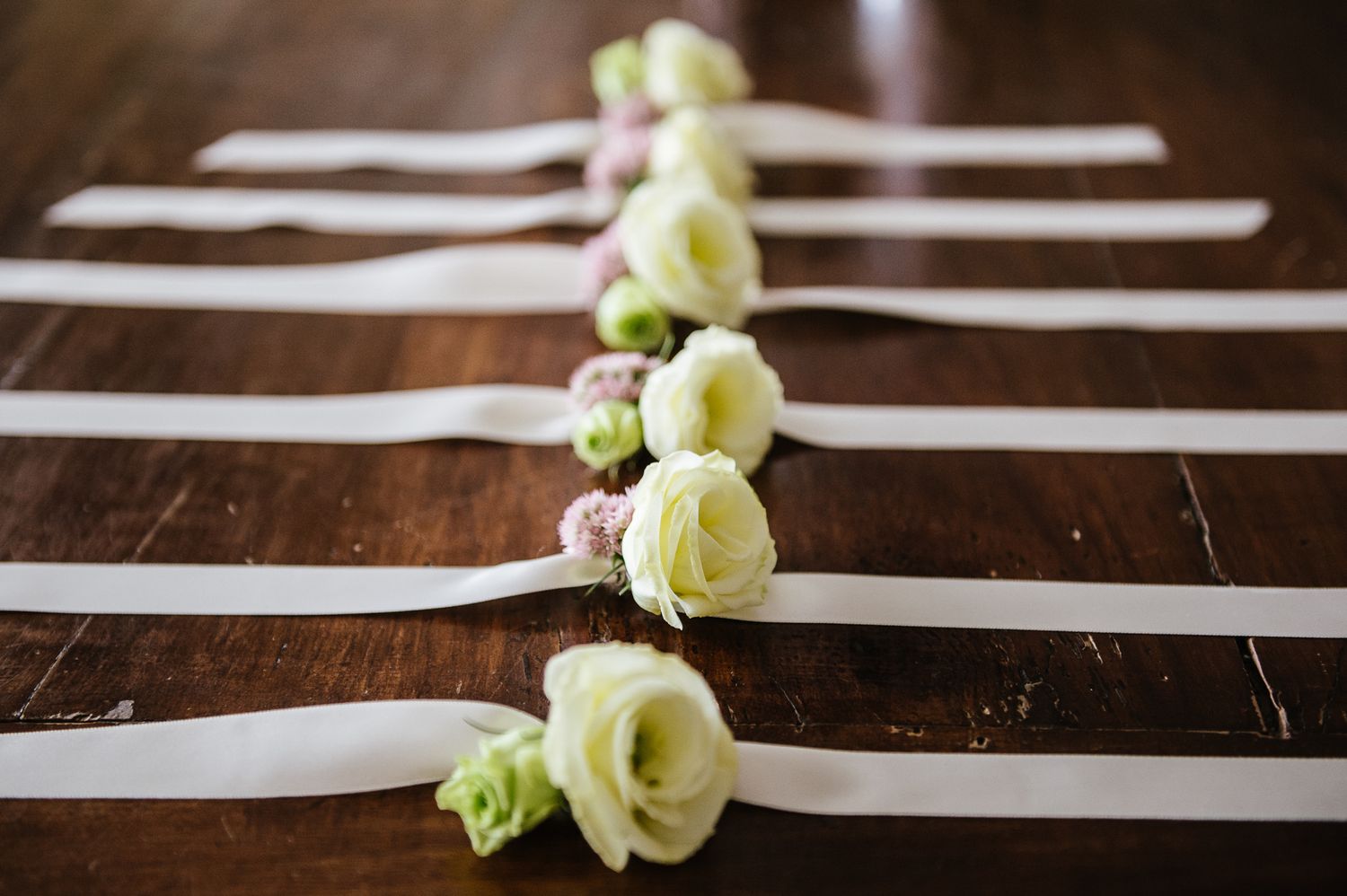 White rose wrist corsages with ribbon on wooden table for wedding bridesmaids.