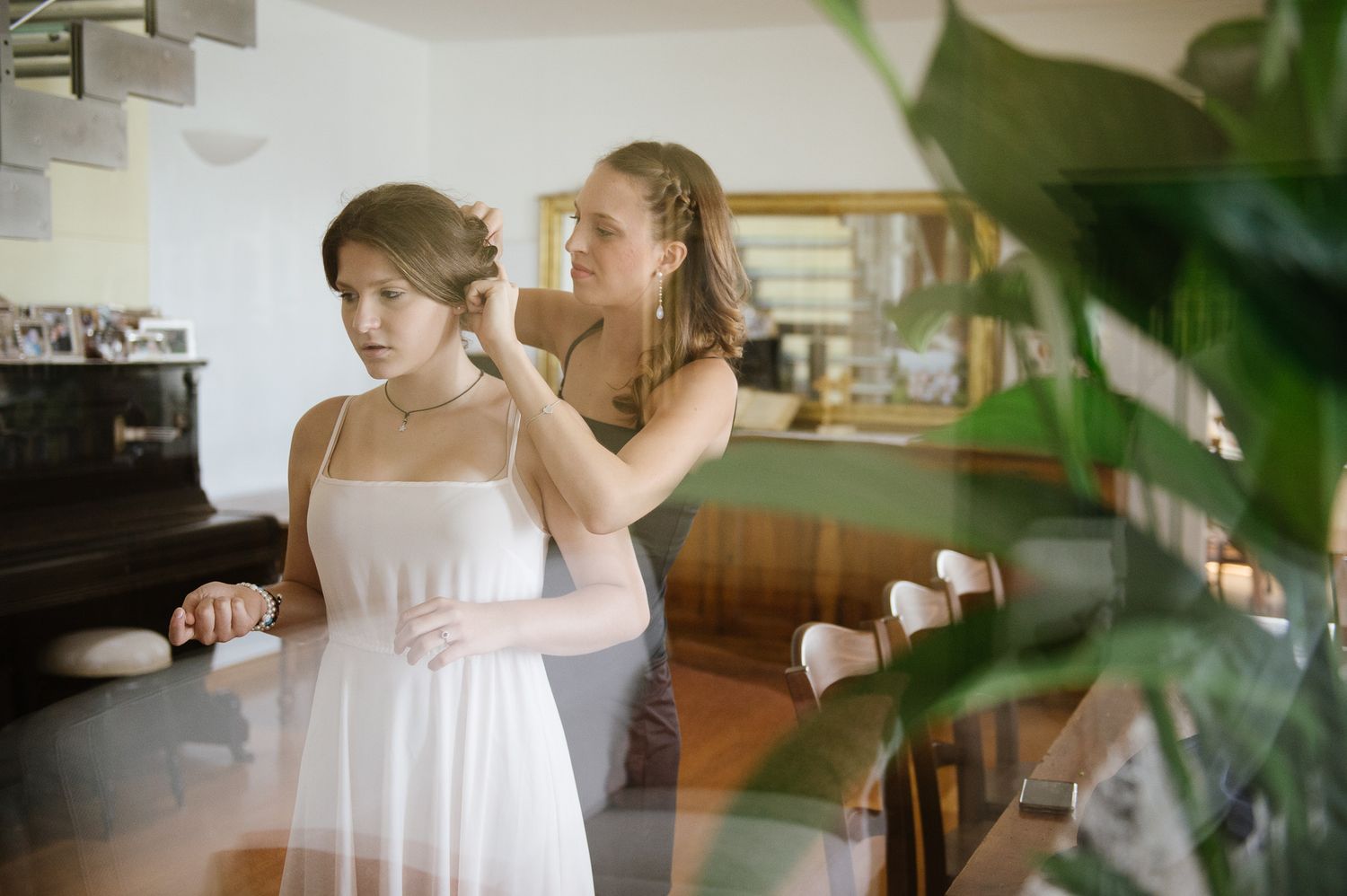Bridesmaid helping bride with hair accessories while wearing white dress before wedding ceremony.