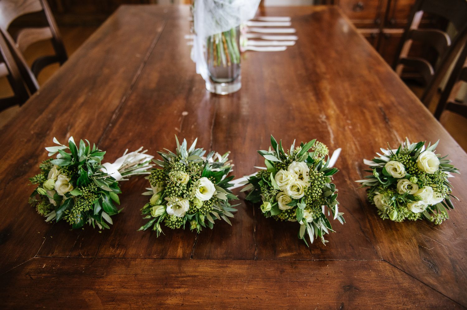 Four green and white wedding bouquets arranged in a row on a rustic wooden table.