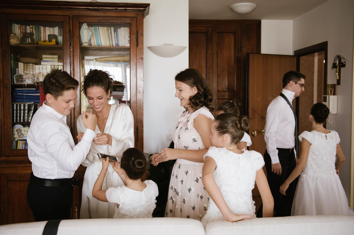 Wedding party getting ready together in elegant room with children and adults in formal attire.