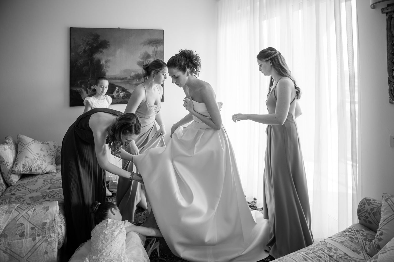 Bridesmaids in gray dresses help bride with white wedding gown in black and white getting ready photo.
