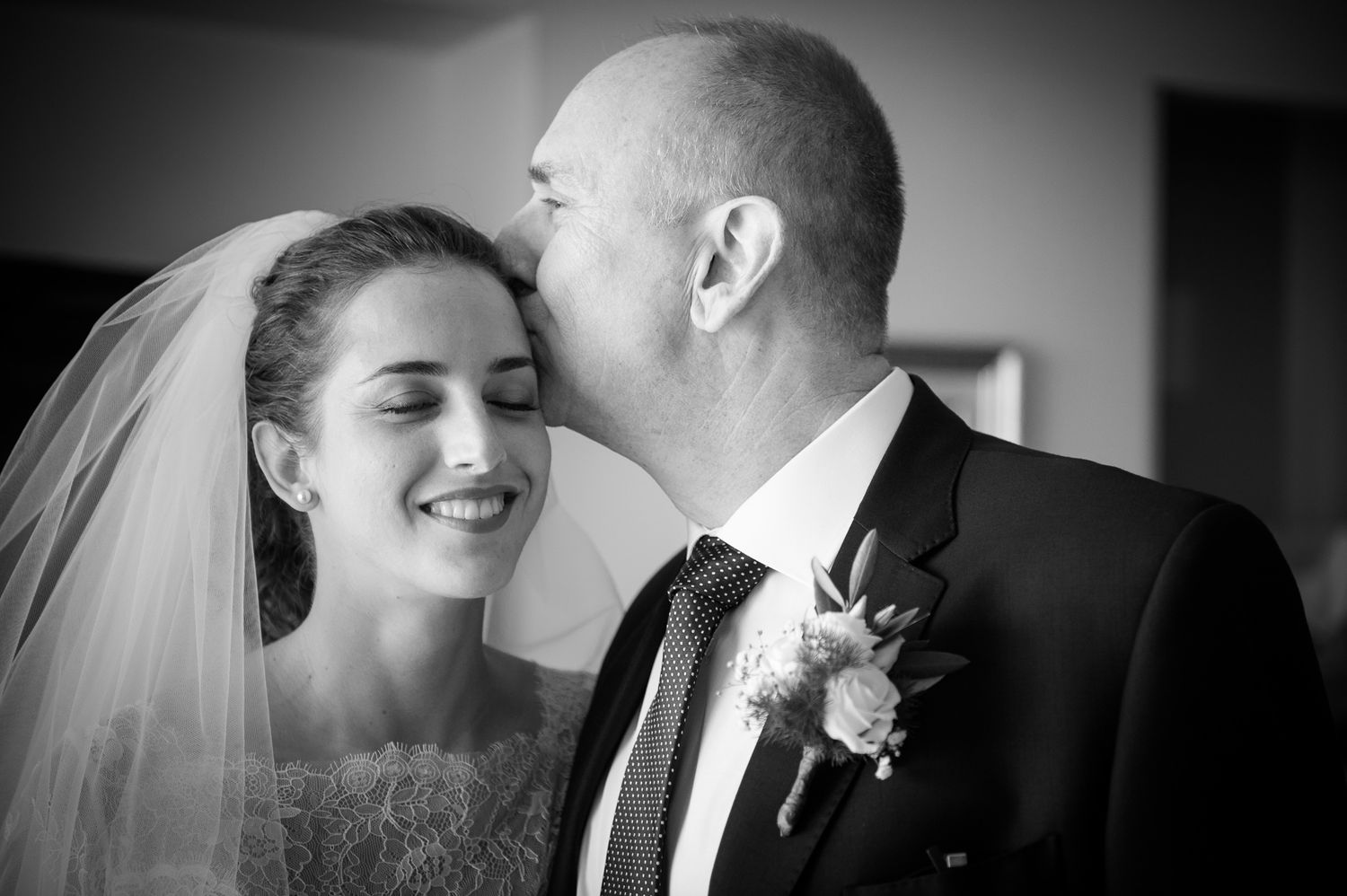 Black and white wedding photo of father kissing bride on the cheek tenderly.