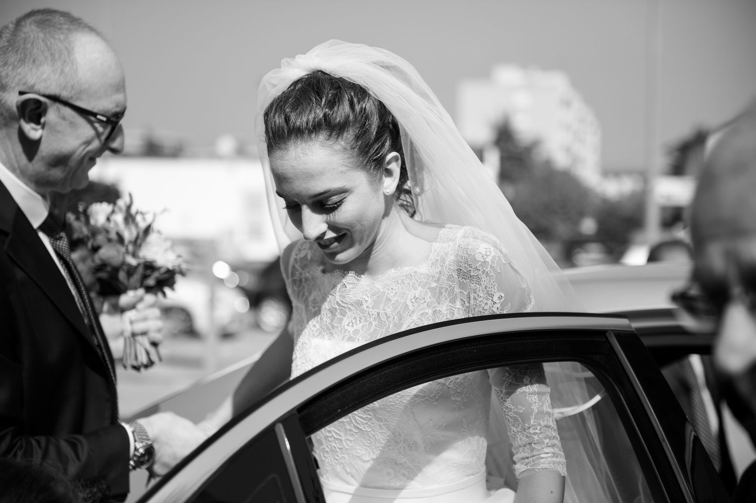 Black and white photo of a bride stepping out of a car on her wedding day.