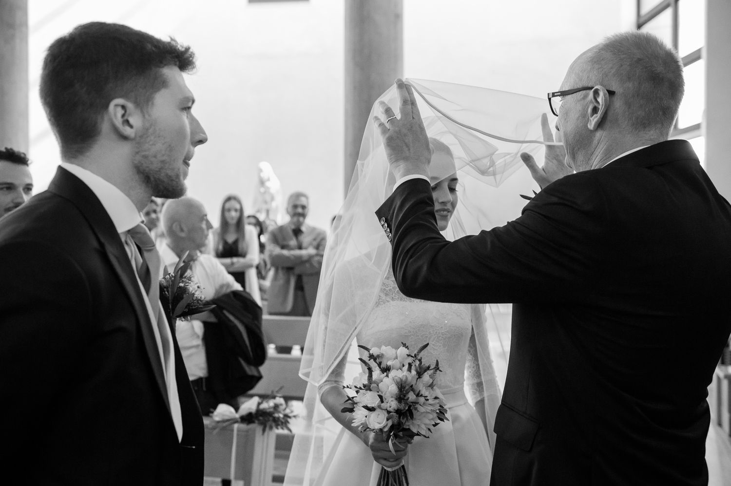 Black and white wedding photo of father lifting bride veil at church altar.