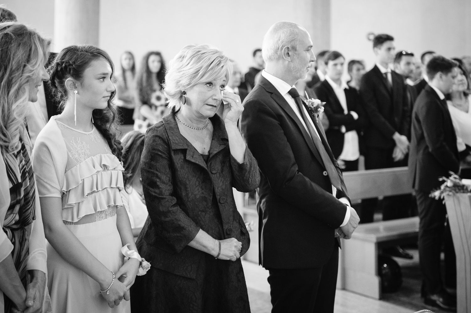 Emotional wedding ceremony guests, including a woman wiping tears, standing in a church aisle during the celebration.