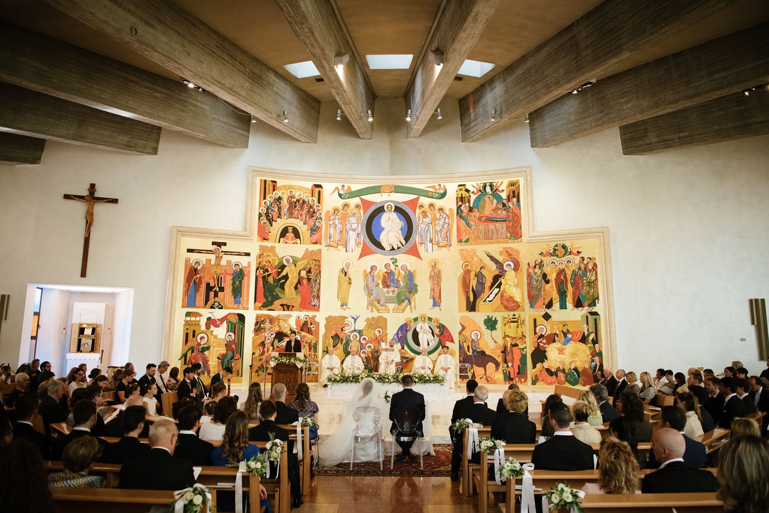 Wedding ceremony inside a modern church featuring a colorful Byzantine-style mosaic altarpiece.
