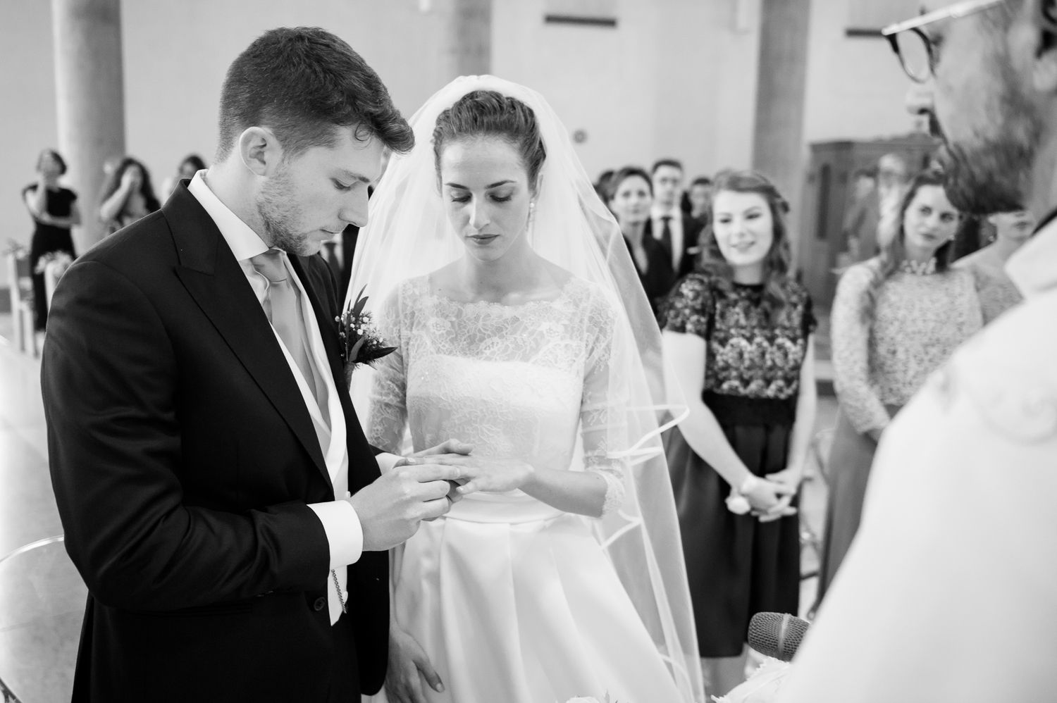 Bride and groom exchanging rings during wedding ceremony in black and white photography.