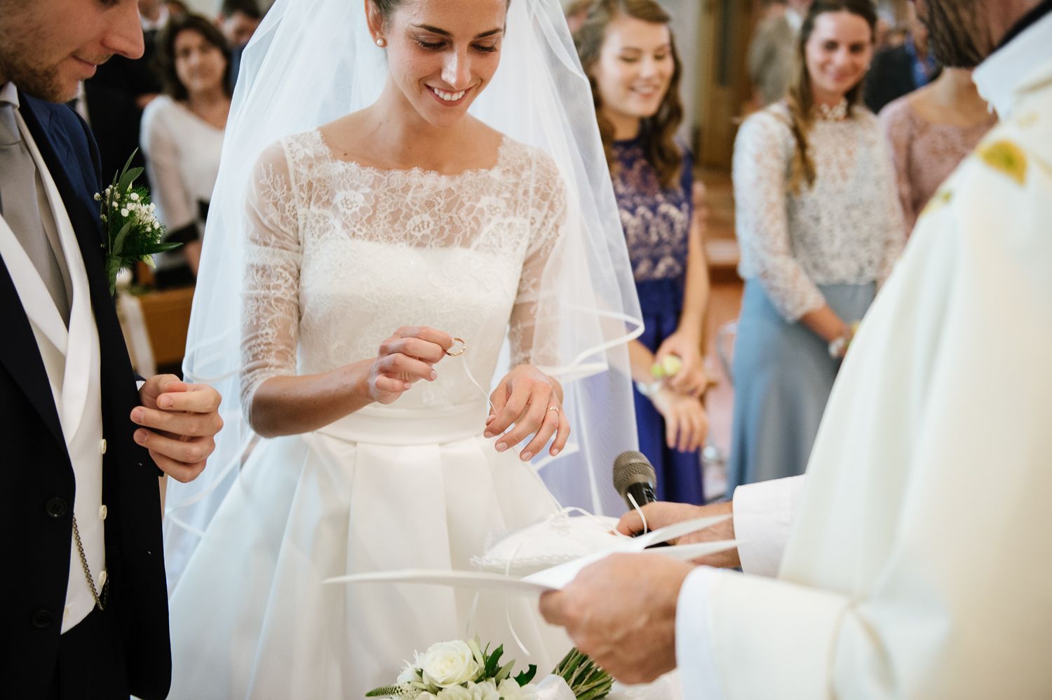 Bride smiling while exchanging rings with groom at a church wedding ceremony.