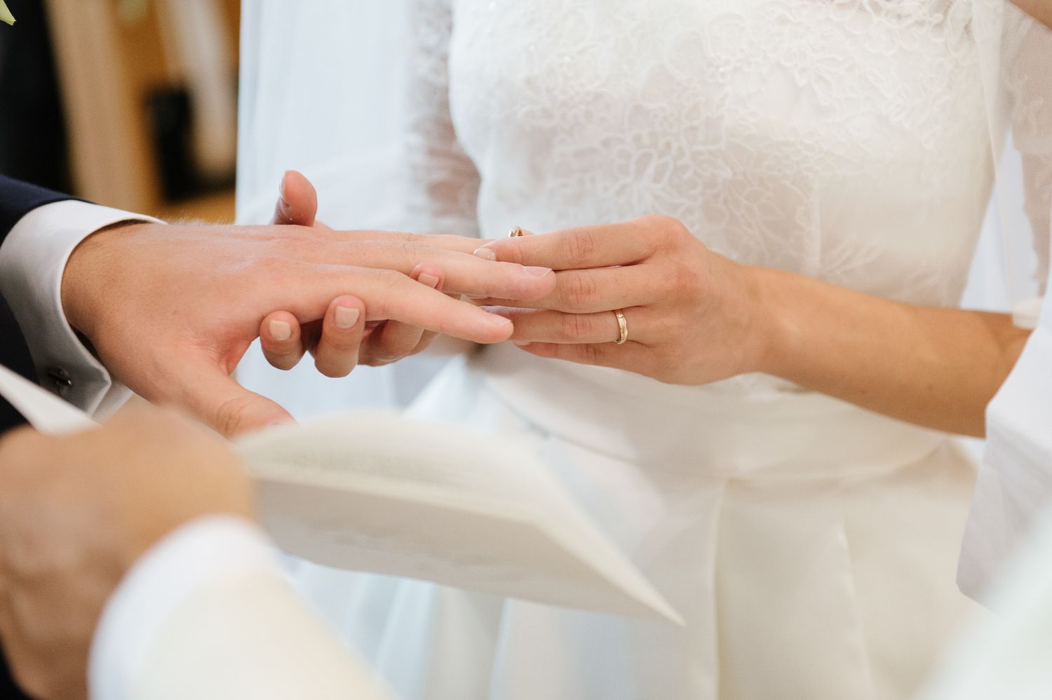 Bride places gold wedding ring on grooms finger during intimate ring exchange ceremony closeup.