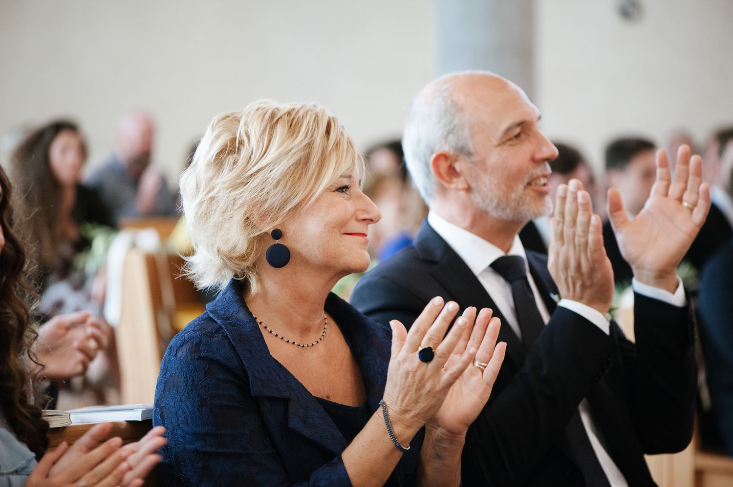 Smiling couple in formal attire applauding at a wedding ceremony.