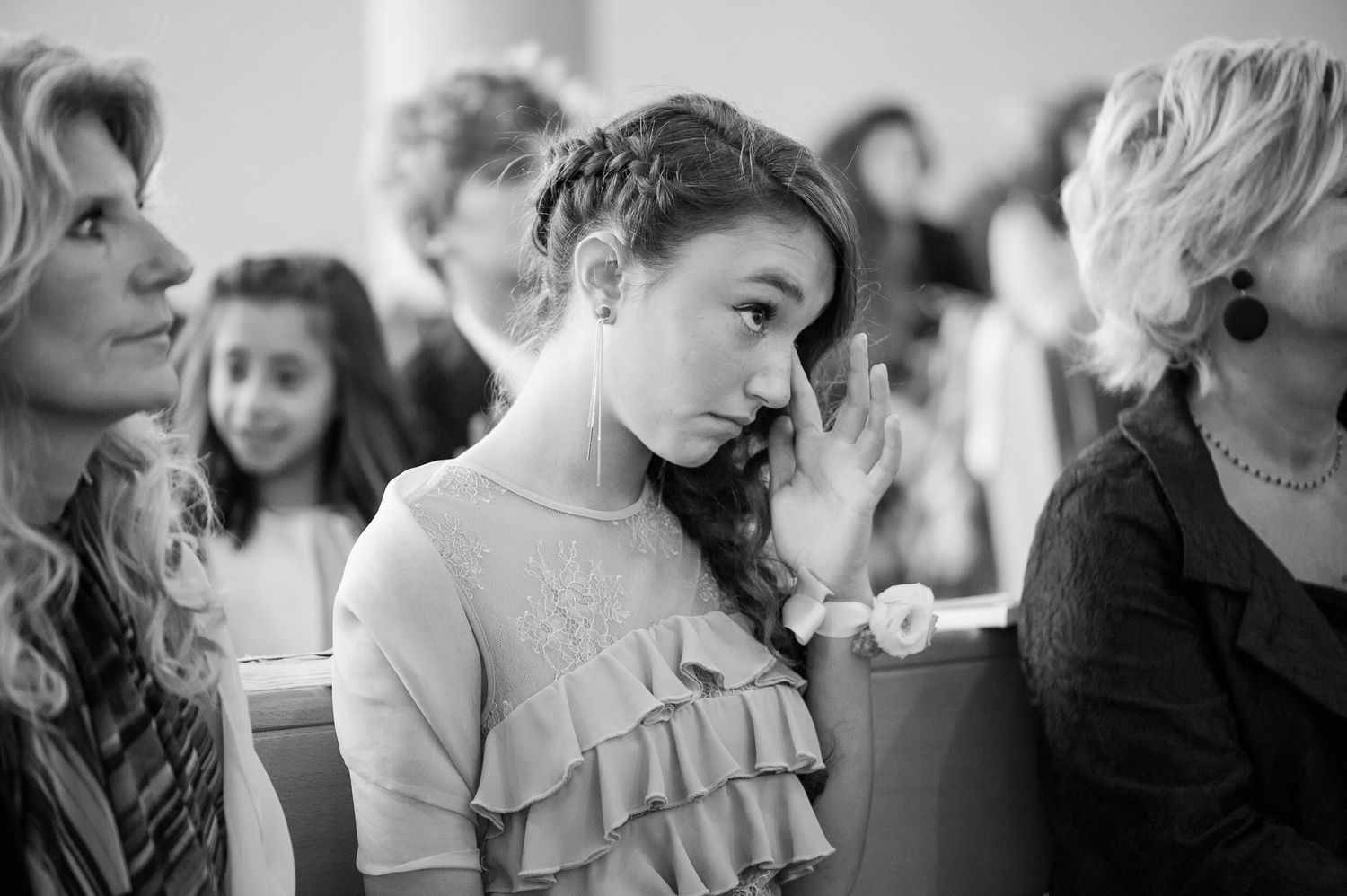 Young girl with braided hair looking emotional during a wedding ceremony in black and white.
