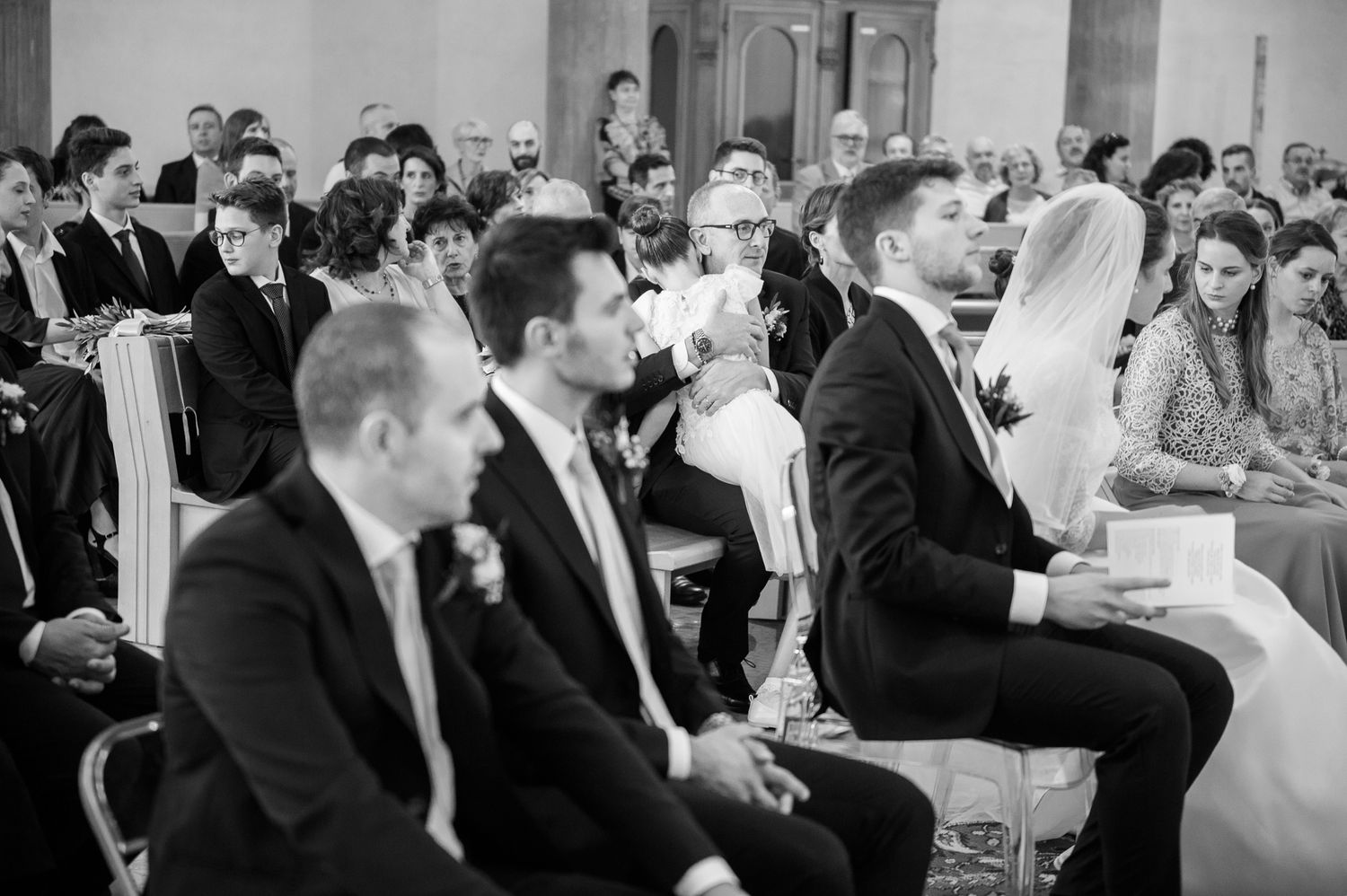 Black and white photo of wedding guests and bridal party seated during a church wedding ceremony.