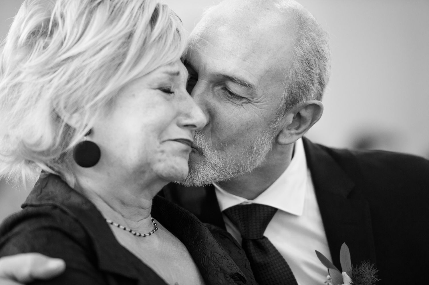 Black and white photo of an older couple sharing a tender kiss at a wedding celebration.