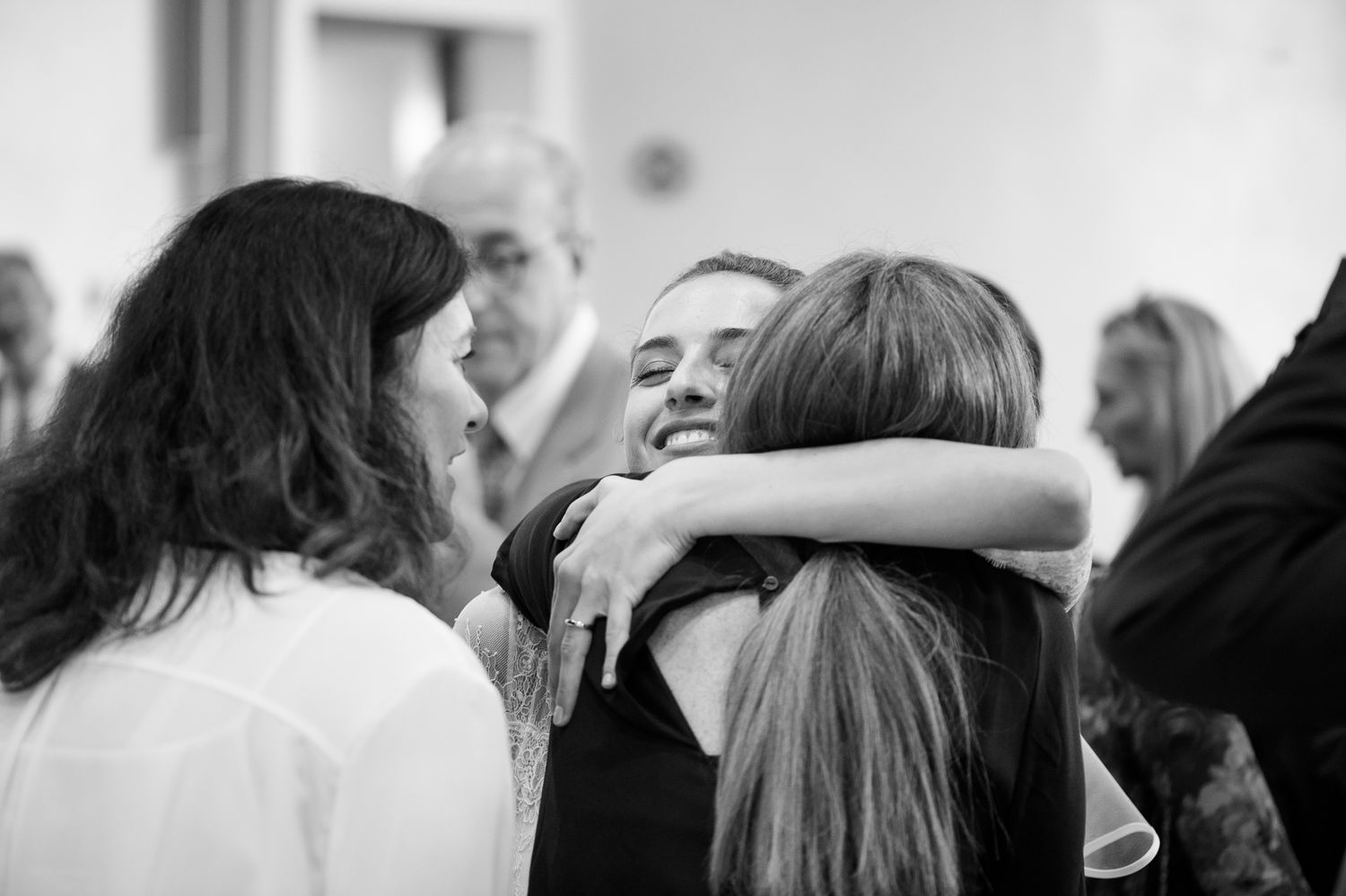 Emotional wedding guests sharing warm hugs and congratulations in black and white photo.