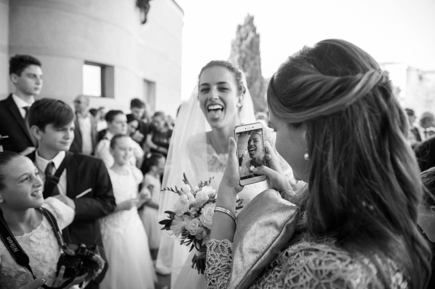 Joyful bride in veil laughing with a guest taking her photo at wedding reception.