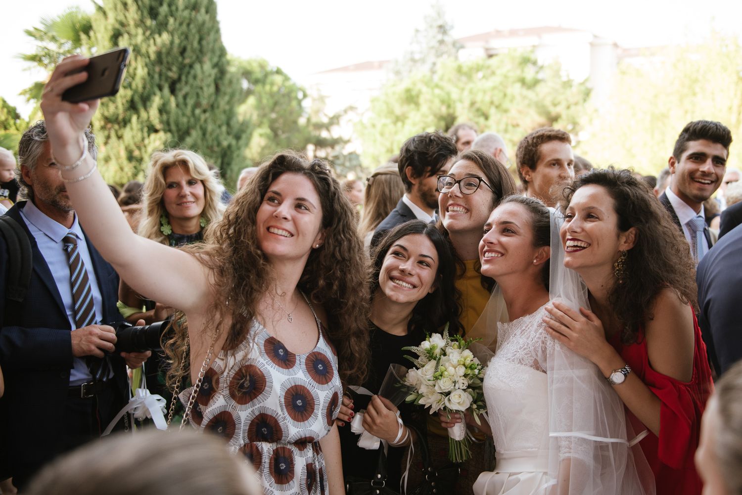 Bride and wedding guests taking selfie outdoors after ceremony celebration.
