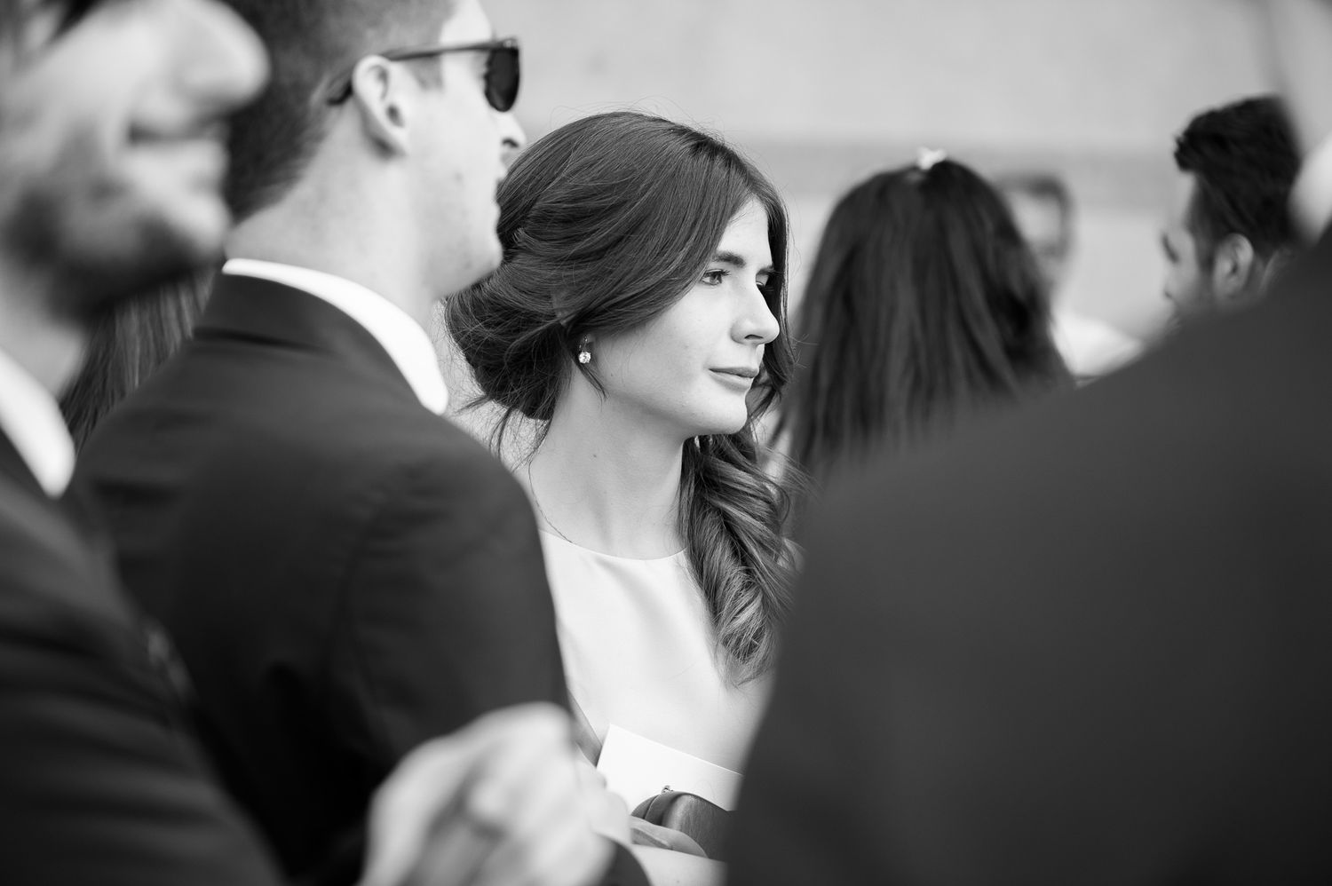 Elegant bride with updo hairstyle glancing sideways among wedding guests in black and white.
