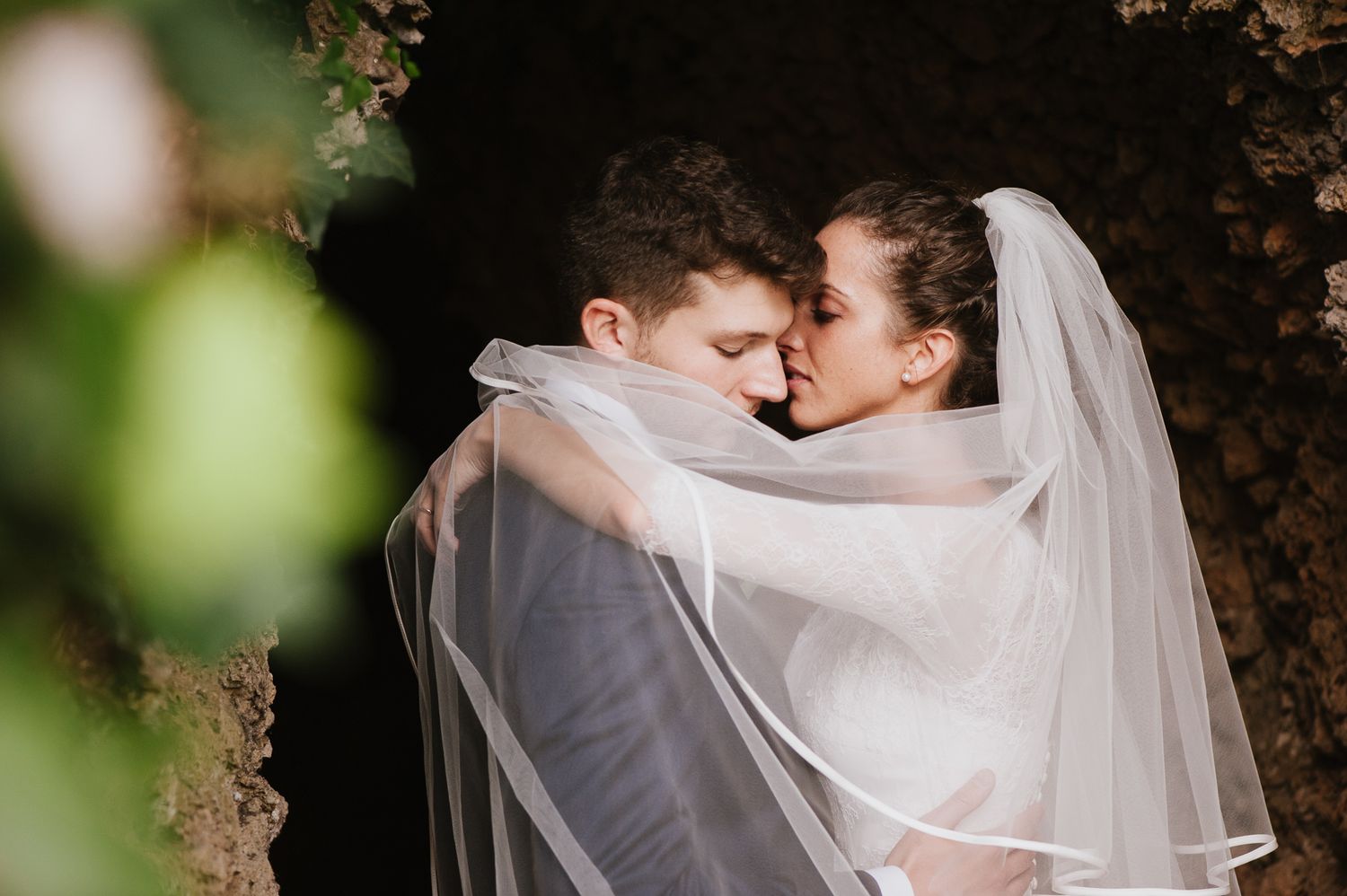 Bride and groom sharing an intimate kiss under a flowing white wedding veil outdoors.