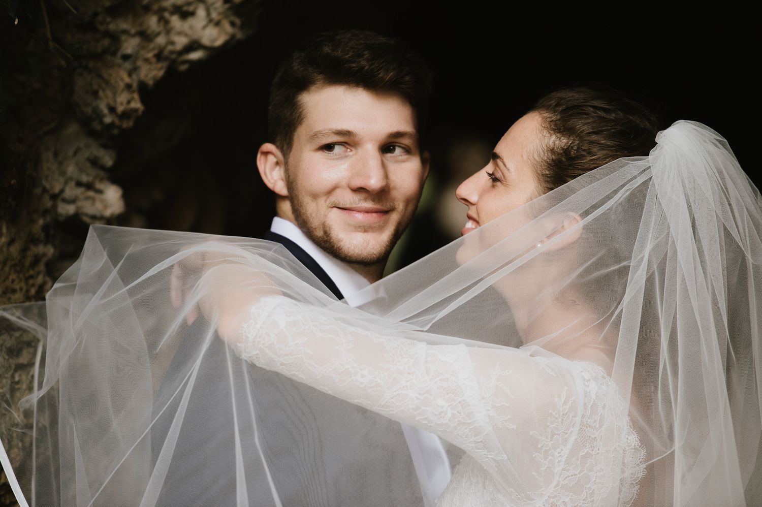 Bride and groom share a romantic moment under a flowing white wedding veil during their ceremony.