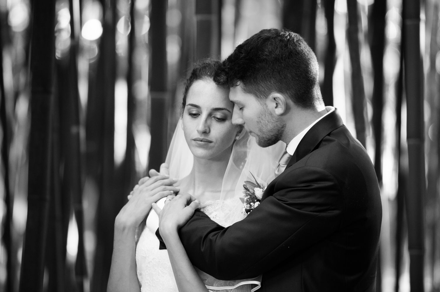 Black and white photo of bride and groom holding hands tenderly in a forest setting.