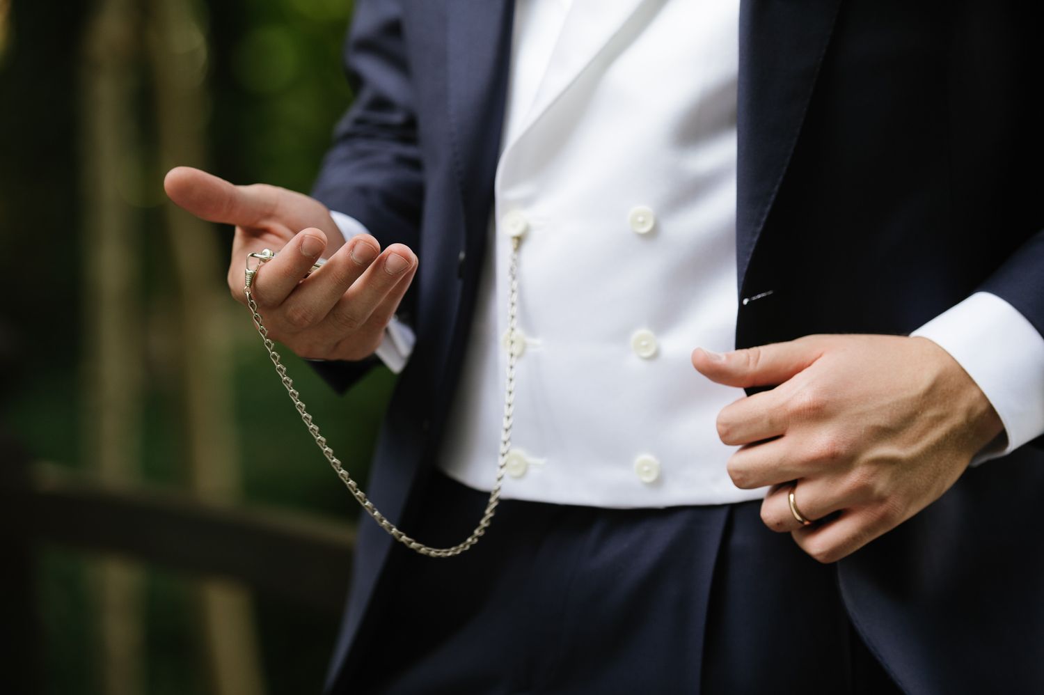 Close-up of groom in dark suit with decorative silver chain and white waistcoat detail.