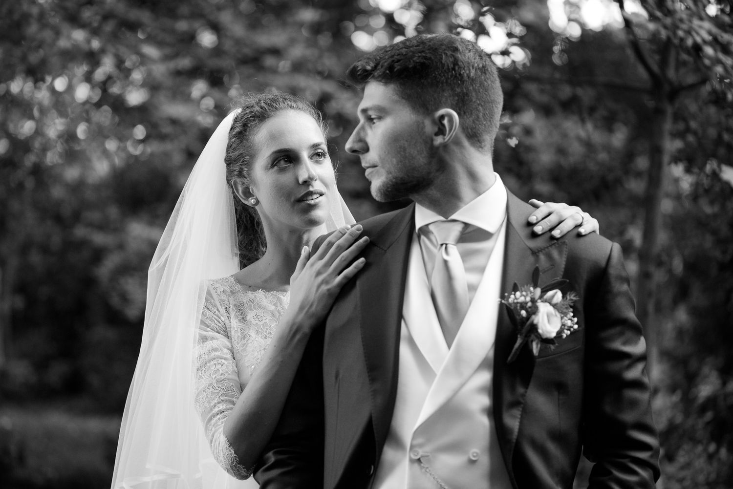Elegant black and white wedding portrait of bride and groom embracing outdoors in a garden.