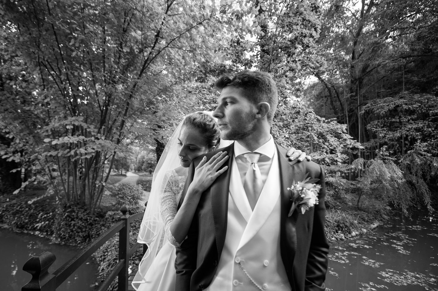 Black and white wedding photo of bride and groom embracing in a lush garden setting.