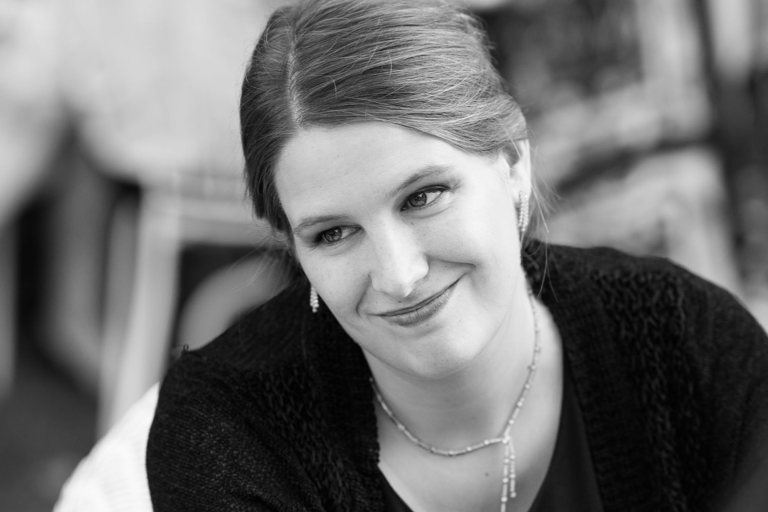 Black and white portrait of a smiling young woman wearing a necklace in a casual setting.