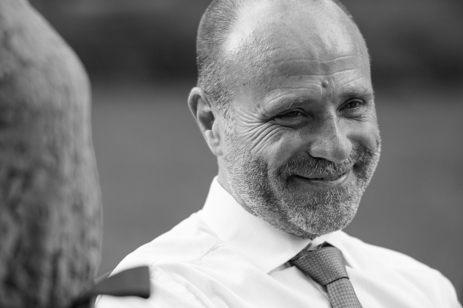 Black and white portrait of a smiling bearded man in a white shirt and tie at a wedding.