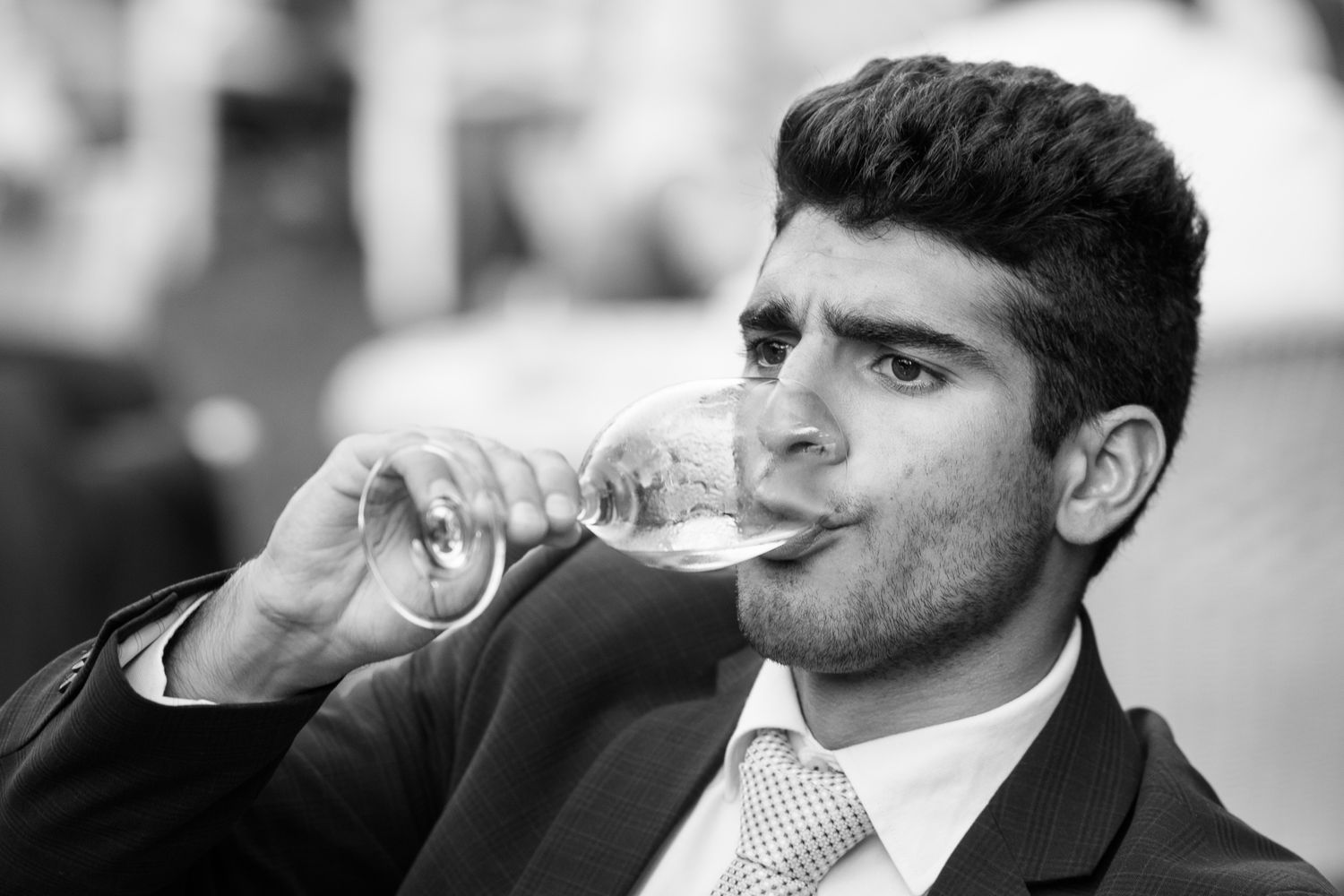 Black and white portrait of a young man in a suit drinking from a wine glass.