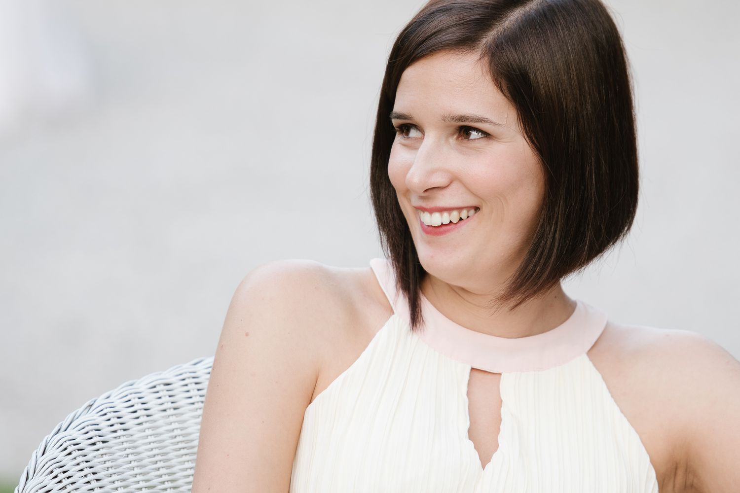 Young woman with short dark bob haircut smiling, wearing a cream halter neck dress in an outdoor setting.