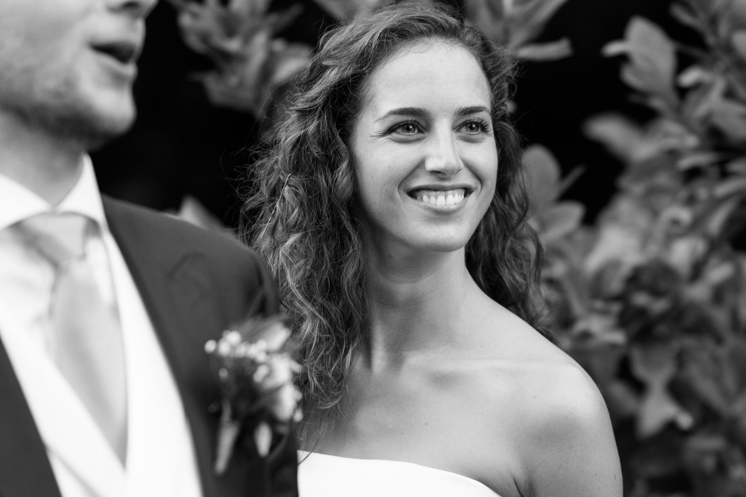 A radiant bride smiles joyfully during her outdoor wedding ceremony in a classic strapless gown.