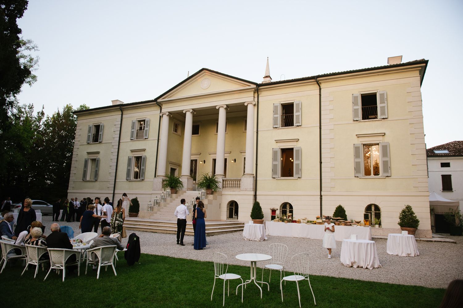 Elegant white villa wedding venue with guests gathered on the terrace at dusk.