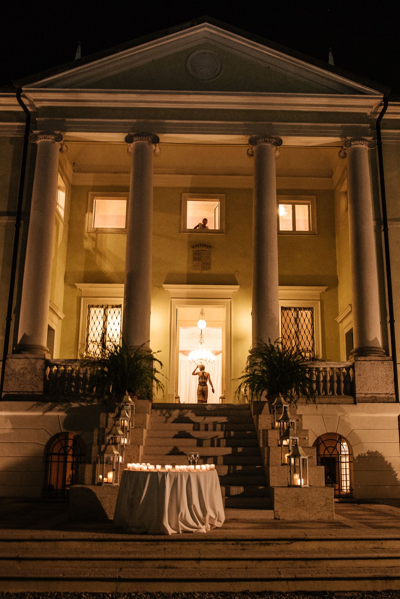 Illuminated neoclassical wedding venue at night with candlelit steps and glowing entrance columns.