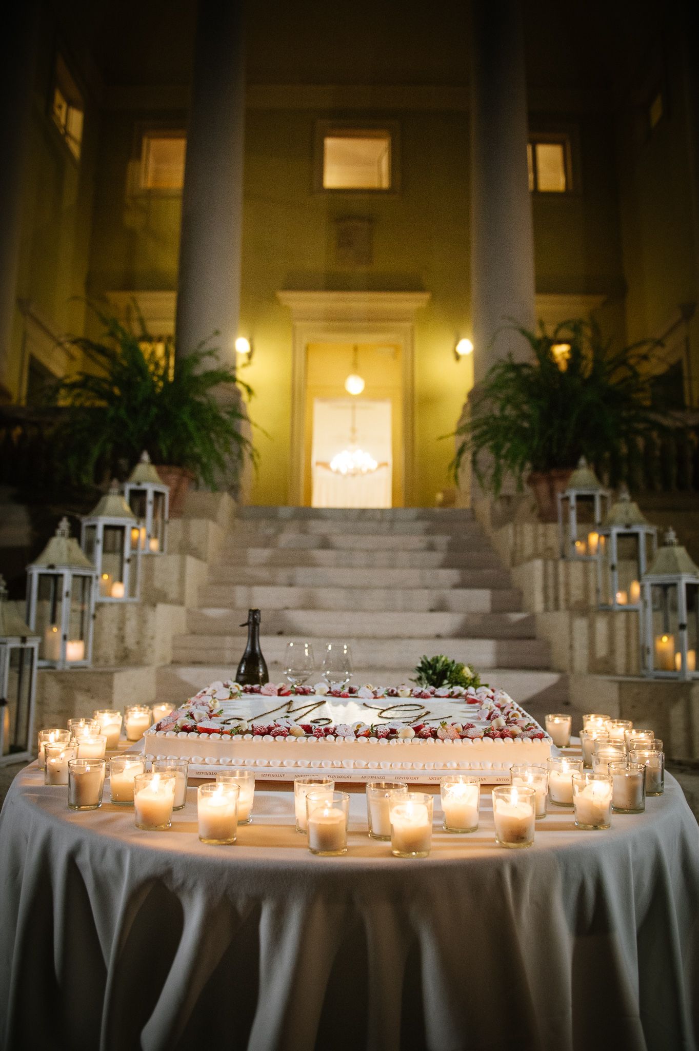 Romantic wedding reception table surrounded by candles at the base of illuminated stone steps.