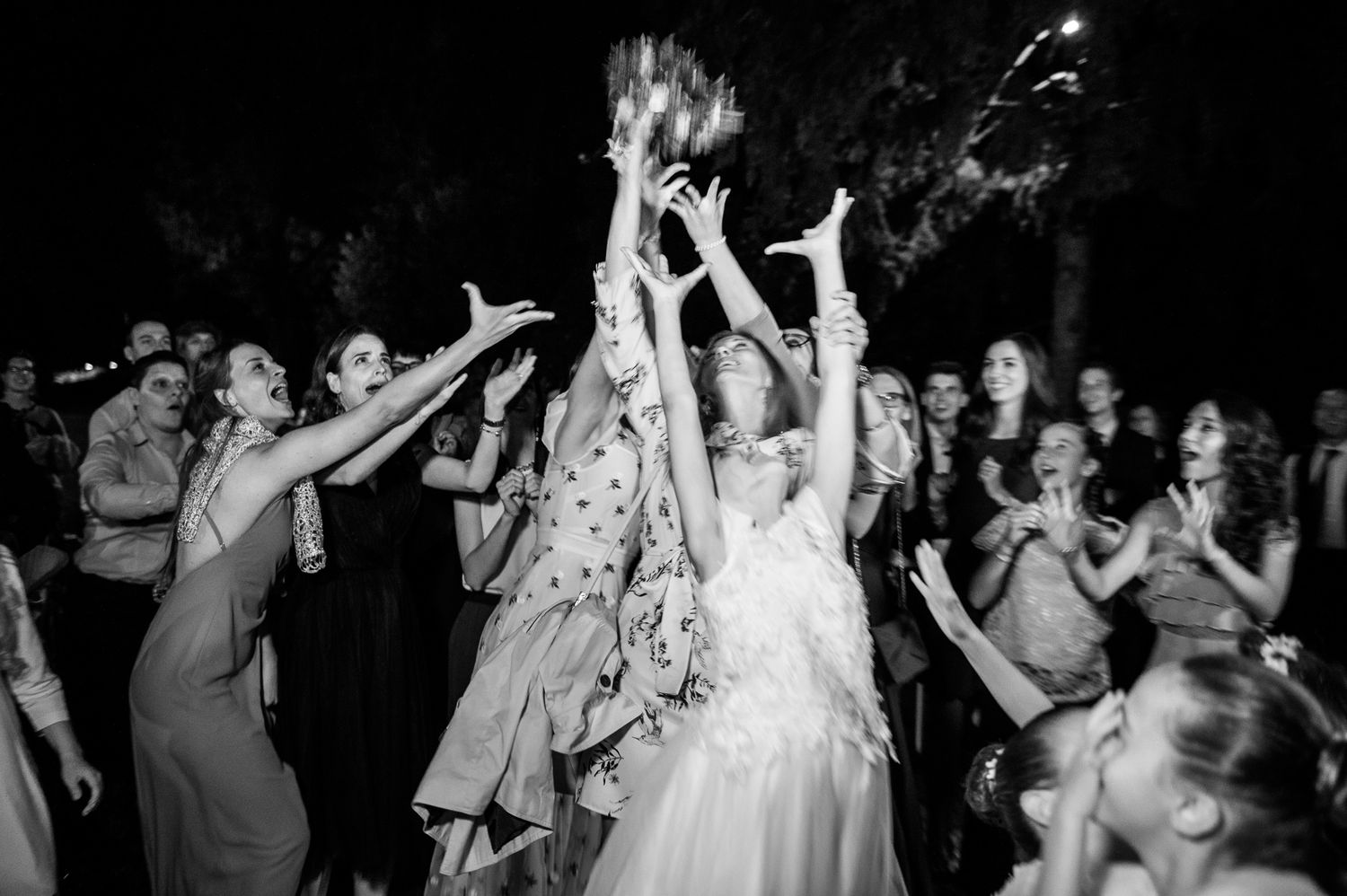 Black and white photo of bride tossing bouquet to excited guests at wedding reception.