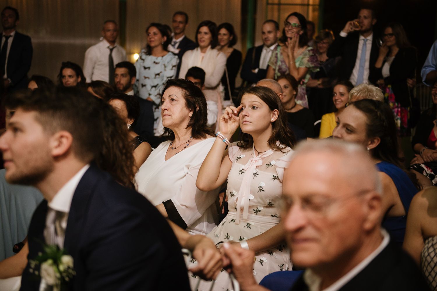 Wedding guests laughing and reacting emotionally during a ceremony in an elegant venue.