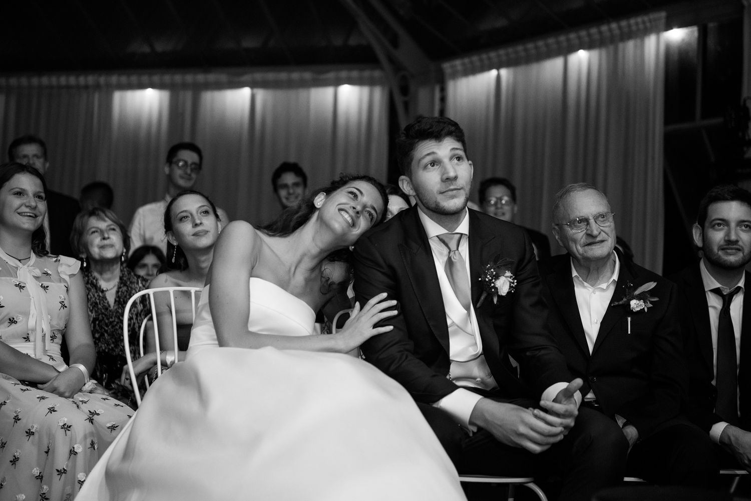 Bride laughing joyfully with groom during wedding ceremony surrounded by guests.