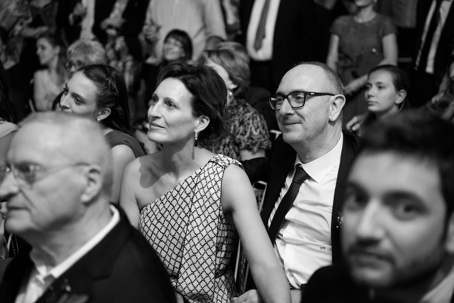 Black and white photo of elegantly dressed couple sitting together at a formal event, smiling and engaged in conversation.
