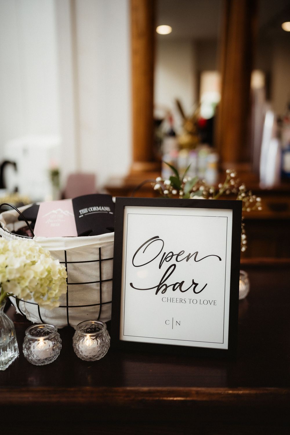Elegant wedding open bar sign reading Cheers to Love in black frame beside white hydrangeas and candles.