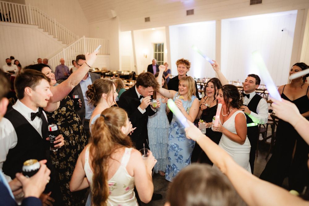 Guests celebrate joyfully on the dance floor at an elegant wedding reception in a white venue.