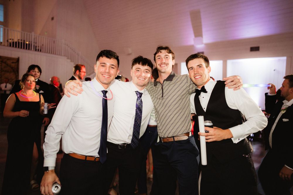 Four young men posing together smiling at a wedding reception venue.