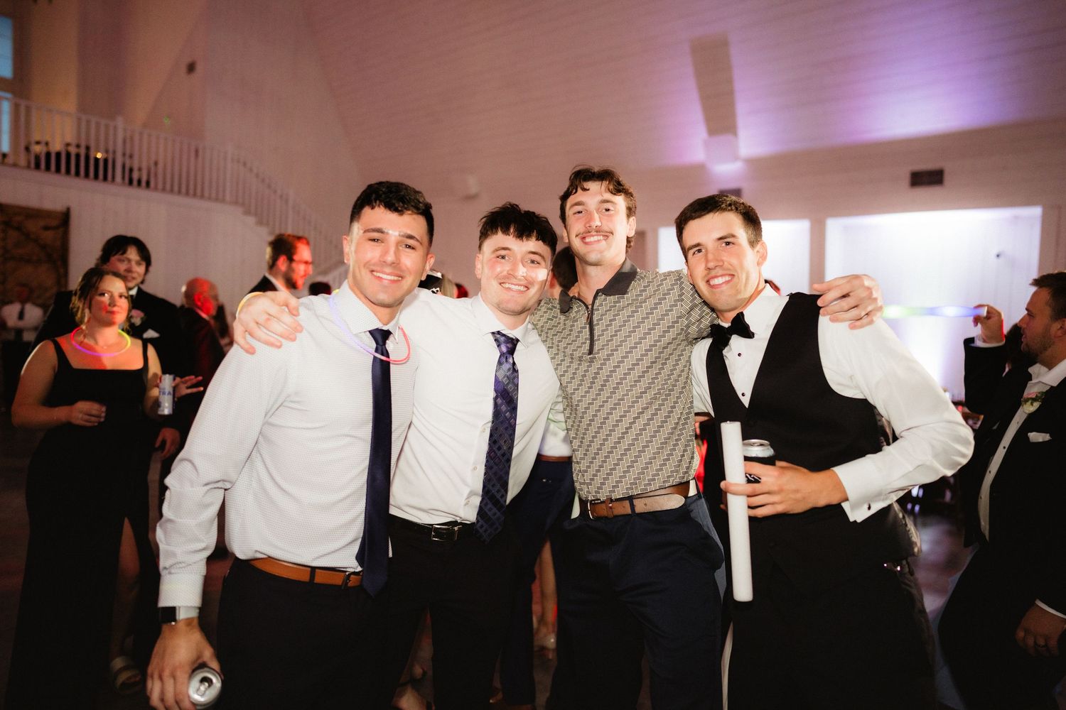 Four young men posing together smiling at a wedding reception venue.