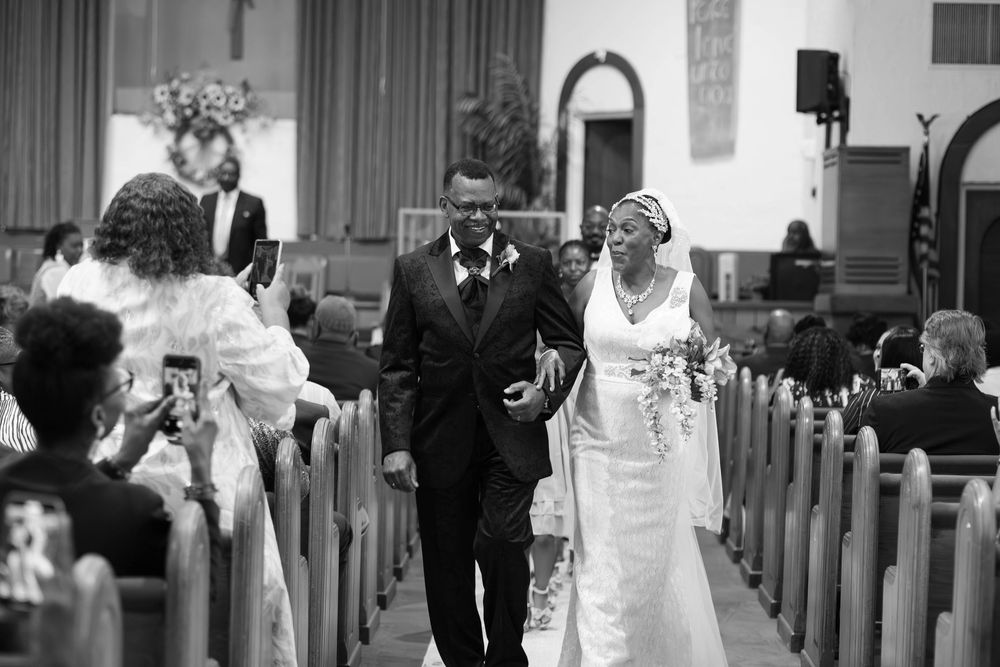 Black and white photo of a bride and groom walking down the church aisle after their wedding ceremony.