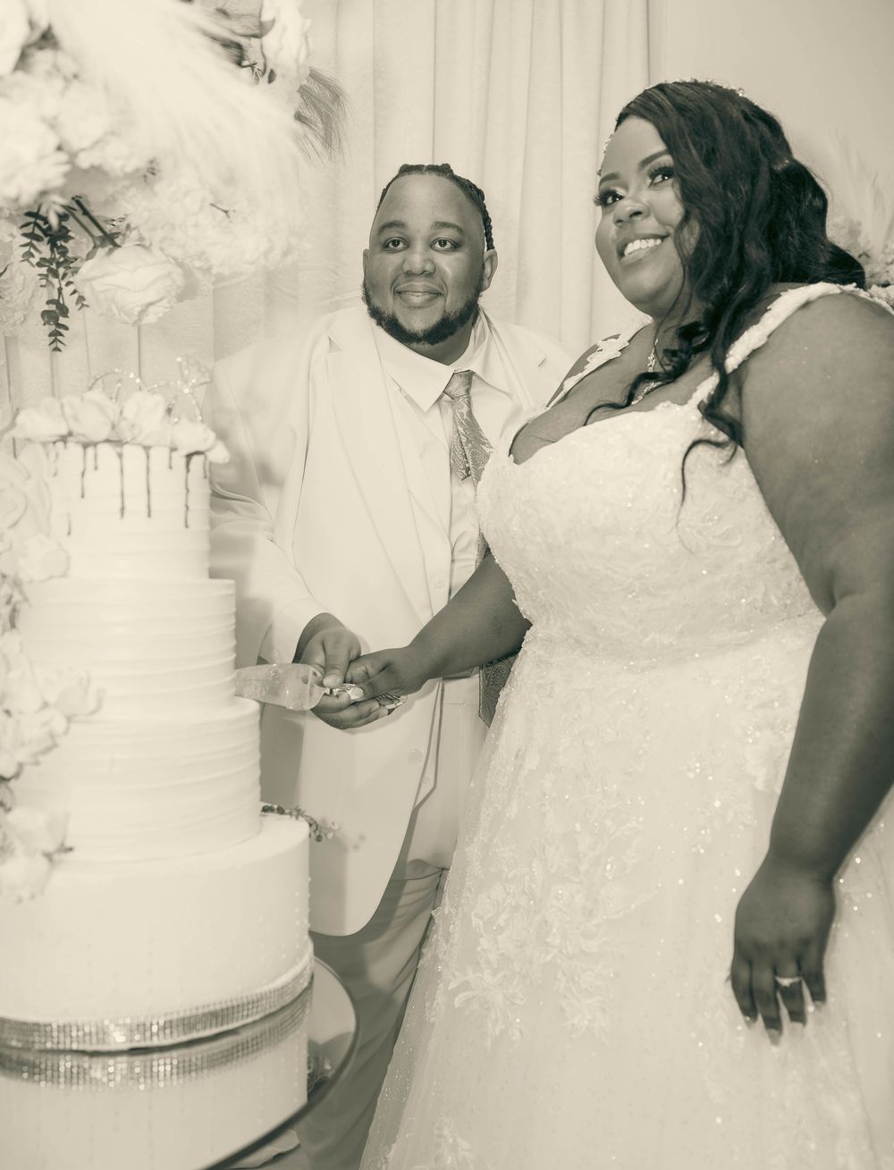 Bride and groom cut tiered white wedding cake at elegant reception in black and white photo.