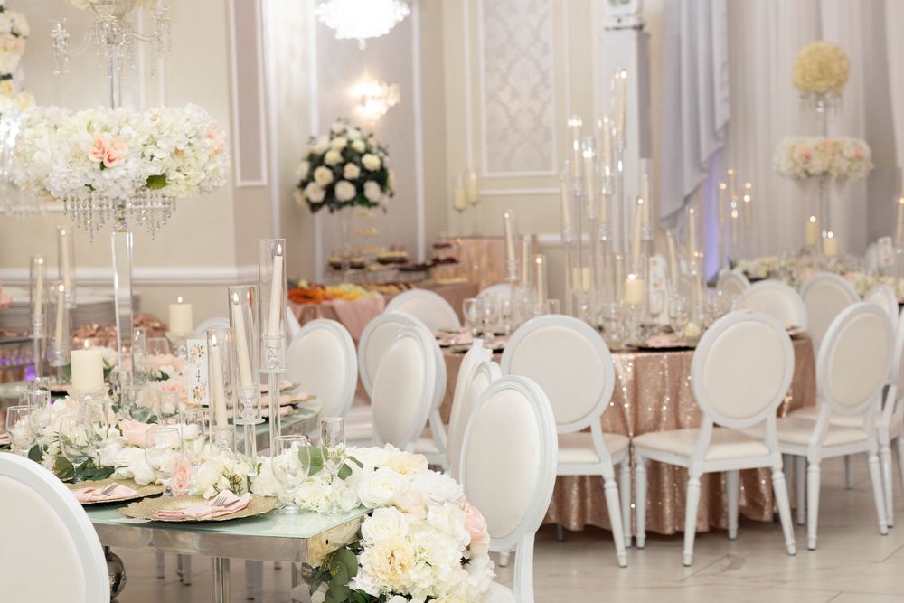 Elegant wedding reception hall with white chairs, crystal candelabras, floral centerpieces, and gold-accented table settings.